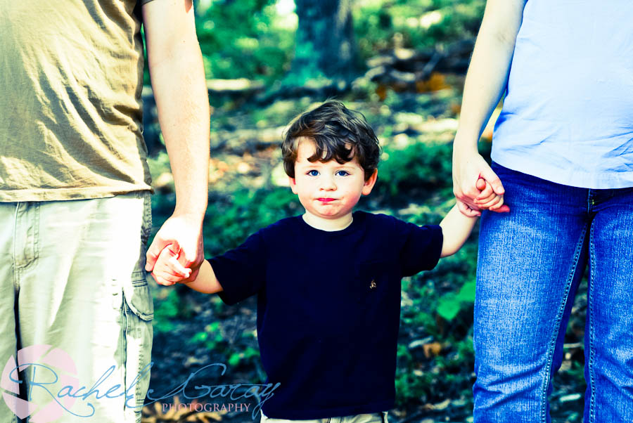 Mother, Father, and Child holding hands in this family portrait outdoors.